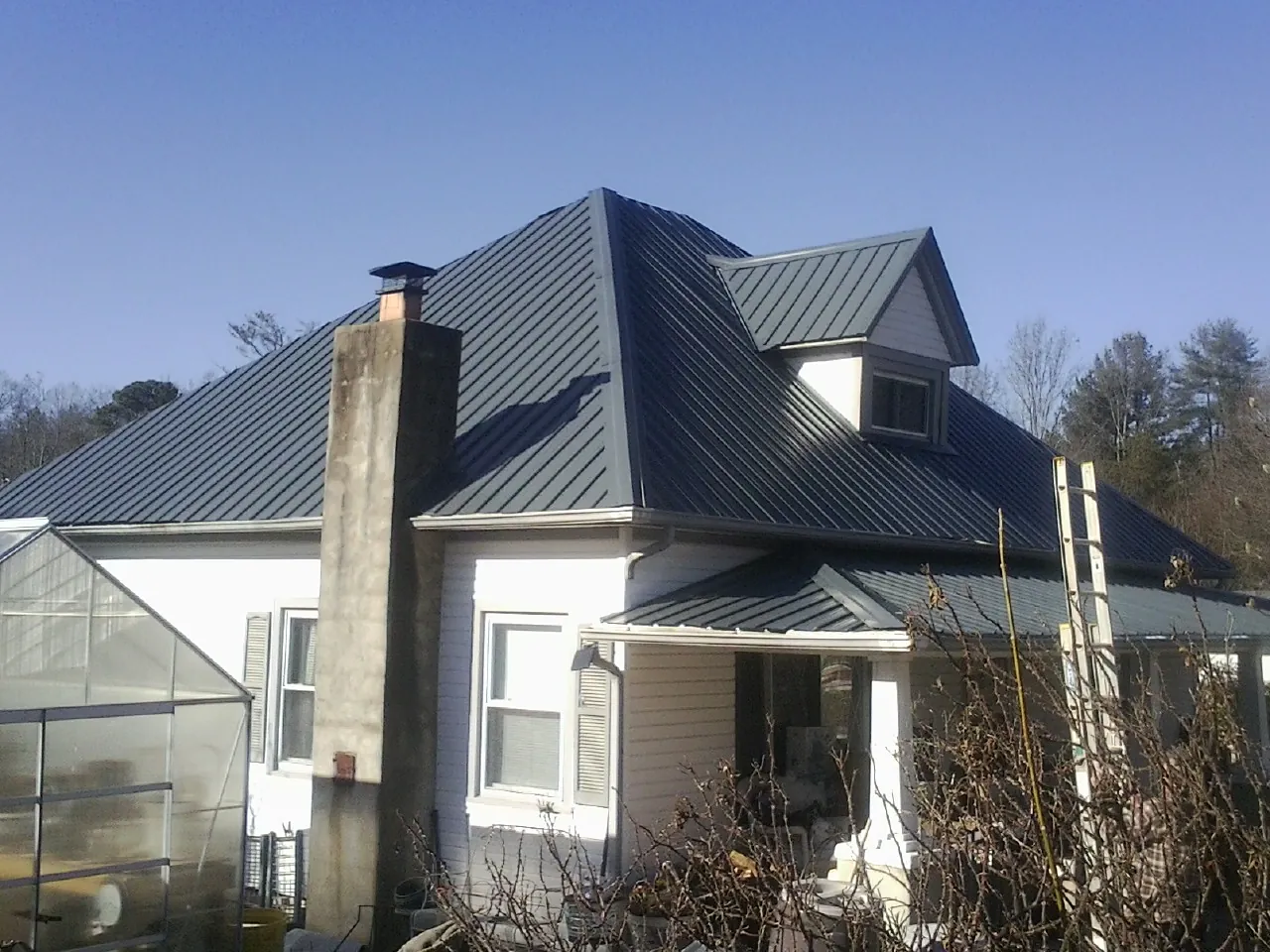 Dark blue standing seam metal roof on a white farmhouse with dormer — Slate & Tile Roof Repair by Roofing Brothers in Gainesville