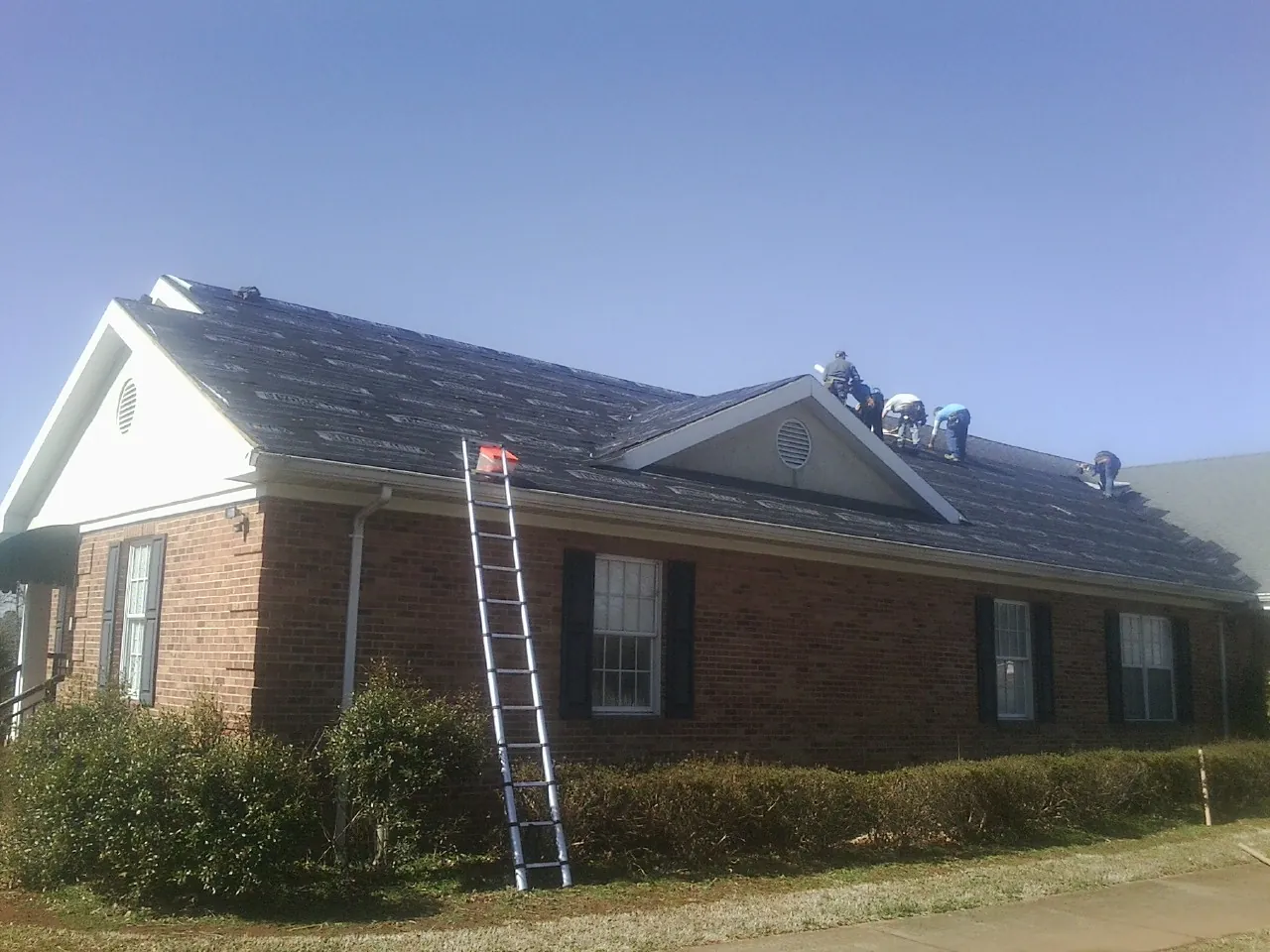 Crew tearing shingles off a brick ranch roof with a ladder set — Metal Roof Repair work by our crew in Gainesville